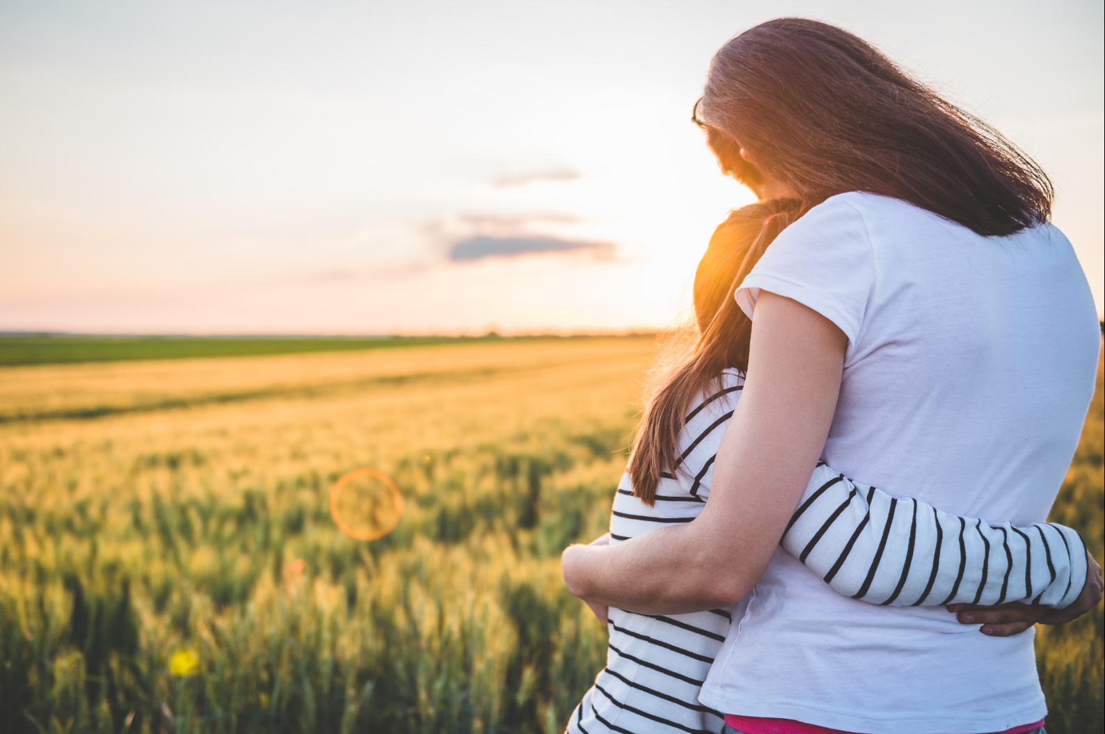 woman hugging daughter in front of a sunrise