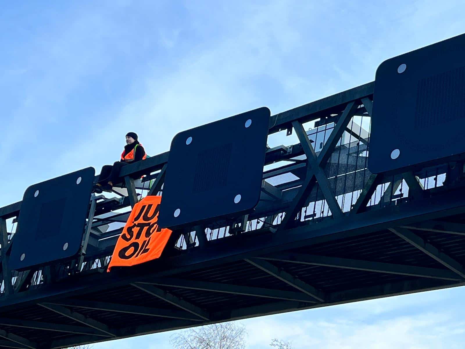 Just Stop Oil Protestor with sign on top of gantry on M25 Motorway