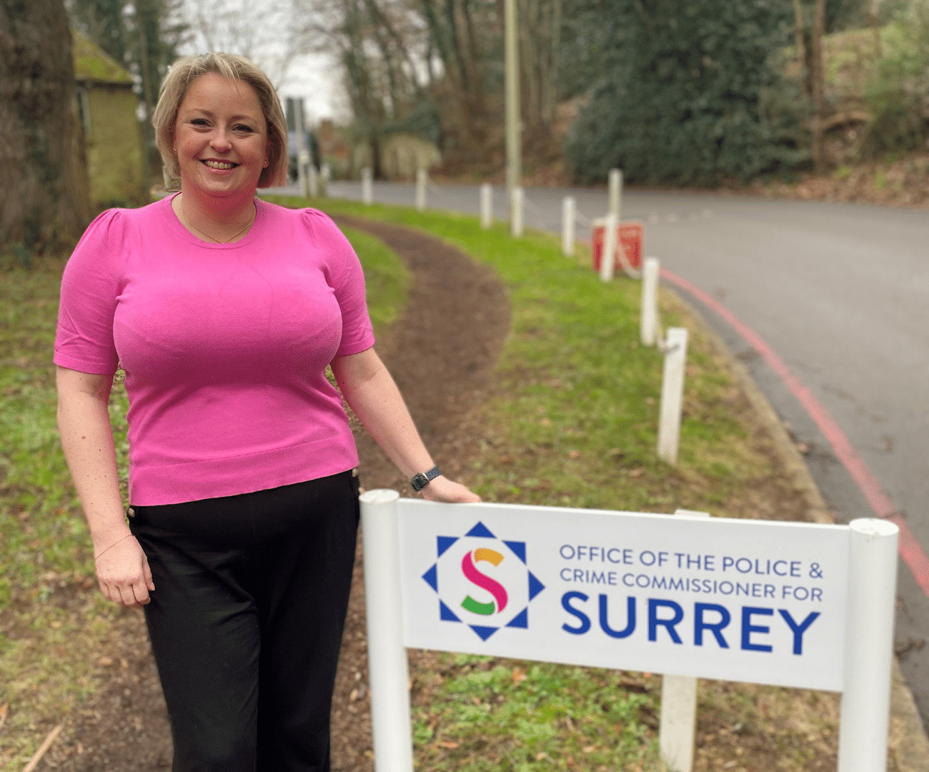 Police and Crime Commissioner Lisa Townsend smiling on sunny day next to sign that says Office of the Police and Crime Commissioner for Surrey.