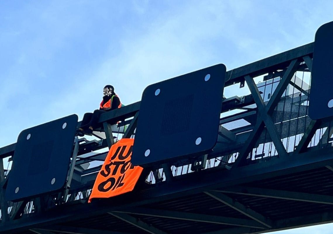 protester hanging Just Stop Oil sign over motorway gantry