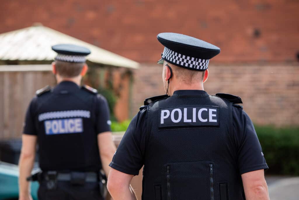 Two Surrey Police special constables in body armour walking towards a shed in a garden as part of a burglary investigation