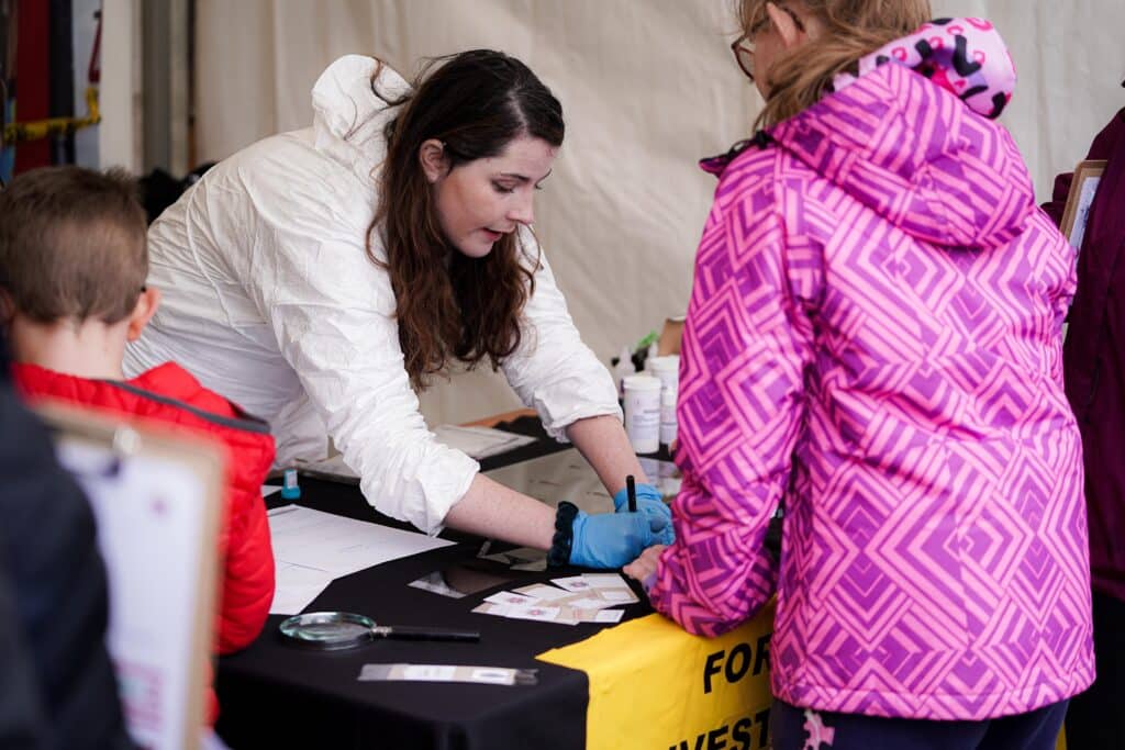 female police staff member in a white forensics suit writing on a piece of card during a demonstration to children during the Surrey Police family open day in 2023