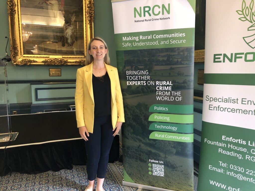 Deputy Commissioner Ellie Vesey-Thompson wears a yellow suit jacket in front of green banner at a conference of the National Rural Crime Network