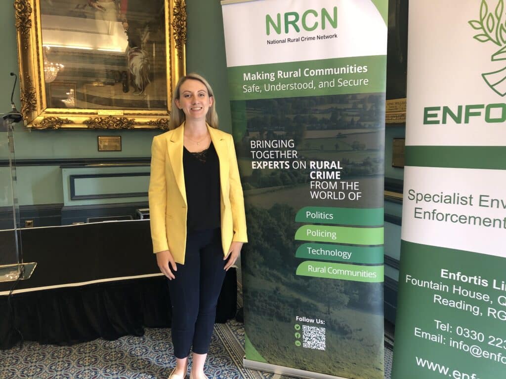 Deputéierte Kommissär Ellie Vesey-Thompson huet eng giel Kostümjacket virum grénge Banner op enger Konferenz vum National Rural Crime Network