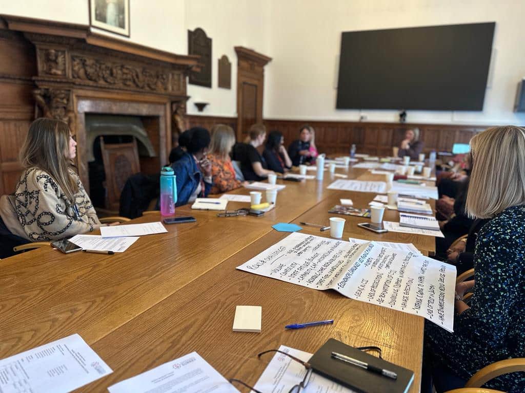 room full of seated women at a wooden table discussing victim care in Surrey. Flipchart paper is visible with notes made in group work during the workshop.