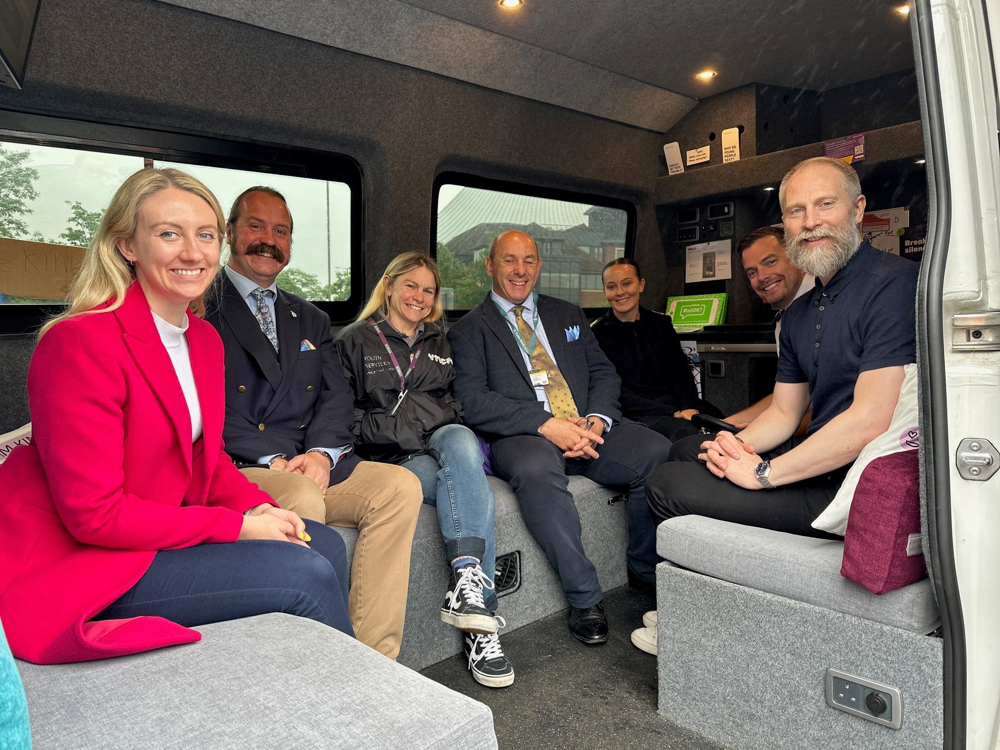 The image shows a group of people sitting inside a van. All are looking at the camera and smiling. The people include Deputy Police and Crime Commissioner Ellie Vesey-Thompson, who sits on the far left and wears a pink coat. It also includes police officers in uniform.